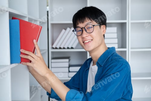Preview: Happy young Asian student pink up books from the bookshelf, preparing for the exam.
