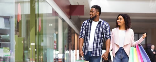 Preview: Seasonal Sales. Happy Black Couple Walking In Mall Center After Buying Clothes