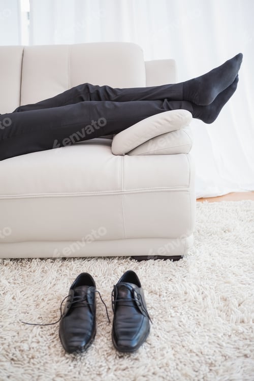Preview: Businessman lying on couch legs only visible at home in the living room