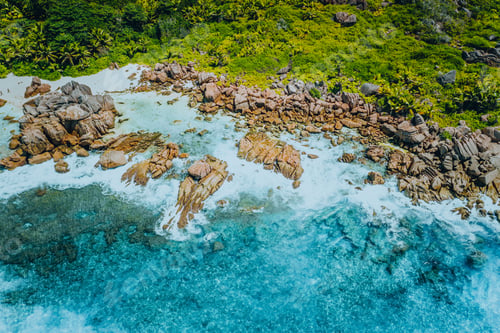 Preview: Aerial top view of beautiful tropical Anse Marron beach. Ocean waves hitting granite rocks along