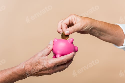 Preview: cropped view of retired man holding pink piggy bank while senior wife putting coin isolated on beige
