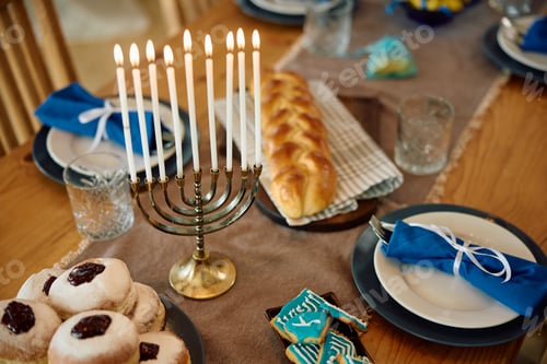 Preview: Decorated dining table with lit candles in menorah for Hanukkah celebration.