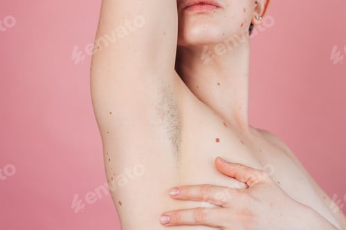 Preview: A young beautiful shirtless woman showing off her hairy armpits on an isolated pink background.