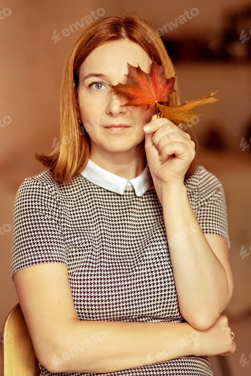 Preview: Portrait of a young woman covering one eye with an autumn fallen maple leaf. Autumn mood