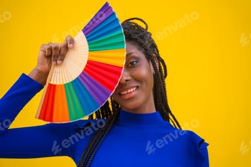 Preview: A black ethnic woman with a rainbow lgbt fan on a yellow background