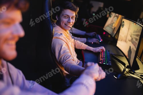 Preview: Smiling man in headset shaking hand of blurred friend near computers in cyber club