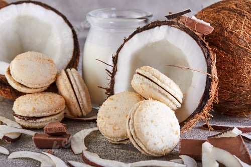 Preview: Coconut macarons with chocolate and coconut flakes on a table with a coconut in the background