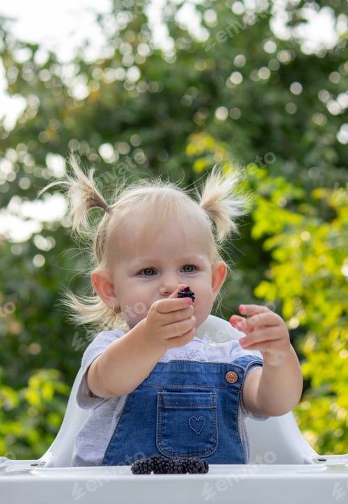 Preview: little happy girl eating blackberry. Selective focus