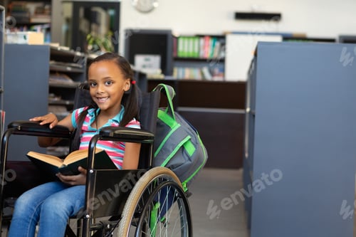 Preview: Front view of a happy disabled mixed-race schoolgirl reading a book in the classroom at school