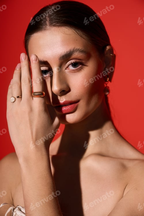 Preview: Captivating young woman poses gracefully against a vivid red background showcasing elegant jewelry