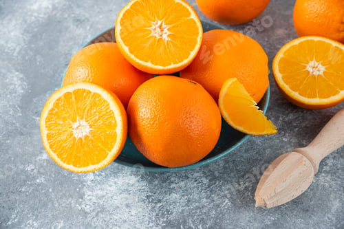 Preview: A bowl full of sliced and whole juicy orange fruits with wooden reamer
