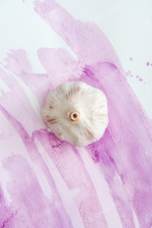 Preview: top view of whole raw garlic on white surface with pink watercolor strokes