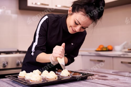 Preview: Woman Decorating Cupcakes in Kitchen with Cream Frosting