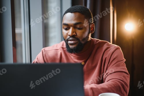 Preview: Portrait of happy african businessman sitting in a cafe and working on laptop.