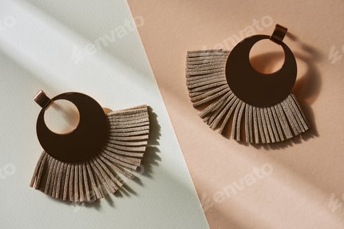 Preview: top view of beautiful luxury brown earrings on beige and white surface with sunlight