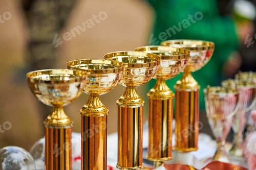 Preview: Champion golden trophies, many shiny golden trophy cups lined up in row on table, trophy awards