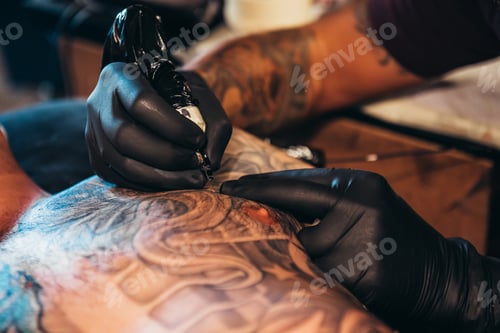 Preview: Tattoo artist hands wearing black gloves while holding a machine