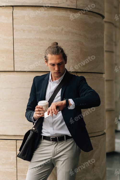 Preview: Young entrepreneur in formal wear holding a coffee and looking on watch