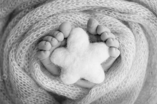 Preview: Knitted star in the legs of a baby. Soft feet of a new born in a wool blanket.