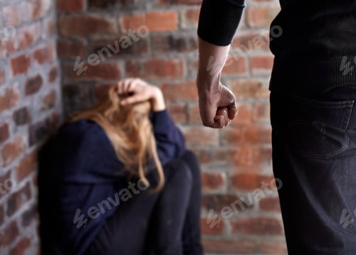 Preview: Trying to hide. Abused young woman with her hands in her hair as her abuser stands in front of her.