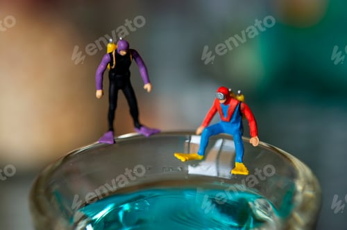 Preview: Tiny Divers Prepare for Adventure, Standing on Edge of Glass Filled with Blue Liquid