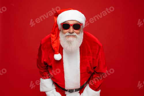 Preview: Close up Santa Claus hat sunglasses looking at camera isolated on red background looking on you