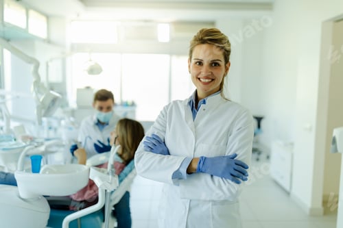 Preview: Dentist female with crossed arms wearing white coat posing and looking at camera.