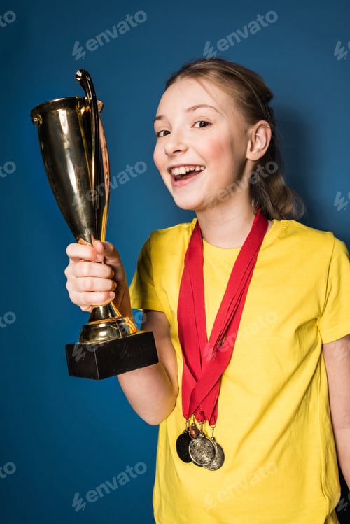 Preview: excited girl with medals and trophy cup isolated on blue