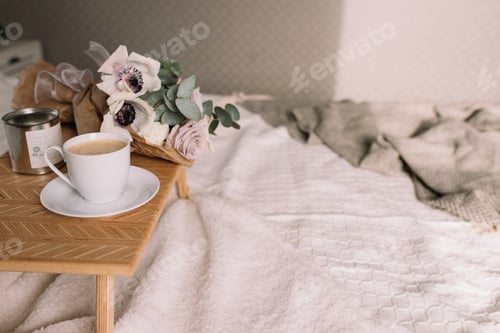 Preview: Coffee table on bed. Flowers, coffee cup and candles. Interior gray tones, plaid