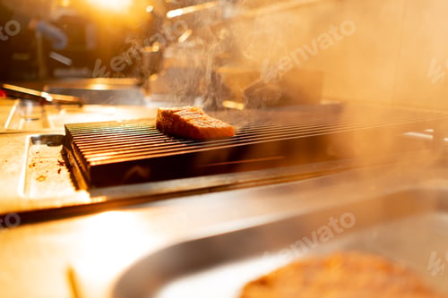 Preview: appetizing juicy raw piece of salmon fish is grilled with smoke in restaurant kitchen