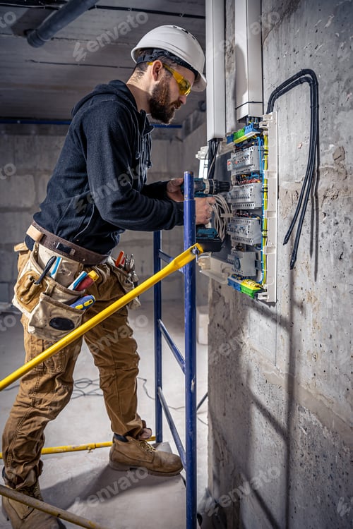 Preview: A male electrician works in a switchboard with an electrical connecting cable.