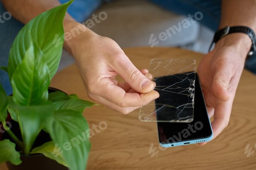 Preview: Man removing cracked protective glass from smartphone at home