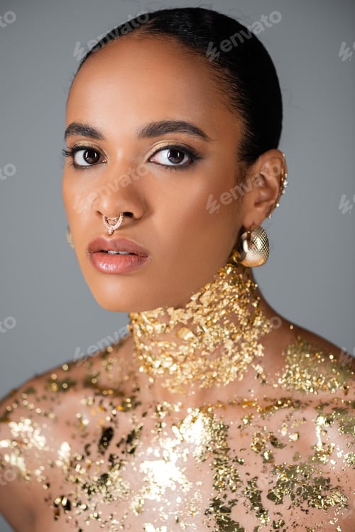Preview: Trendy african american woman with golden accessories and foil on chest isolated on grey
