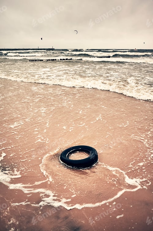Preview: Old black rubber tire left on a beach.