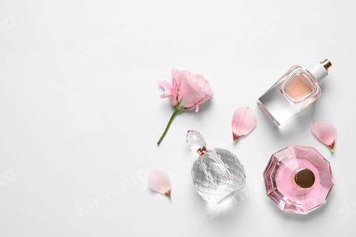 Vista previa: Different perfume bottles and flowers on white background, top view