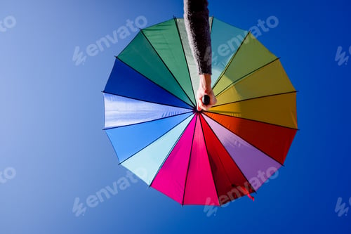 Preview: Woman holds an umbrella of vibrant colors with the background of a clear blue sky.