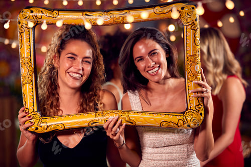 Preview: Female Friends Having Fun Posing With Photo Booth Photo Frame At Party In Bar