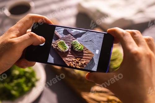 Preview: Smartphone taking picture from organic healthy sandwiches with avocado. Man hand.
