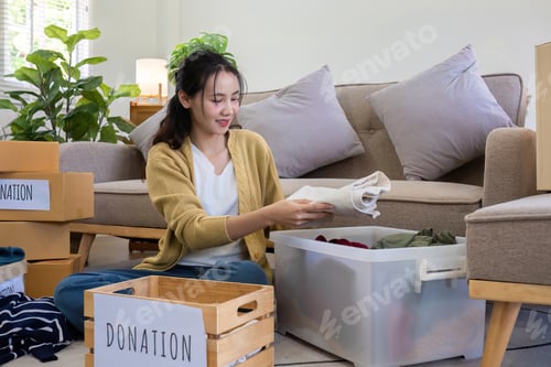 Preview: A young Asian woman sits on a sofa sorting unwanted clothes to donate to a charity.