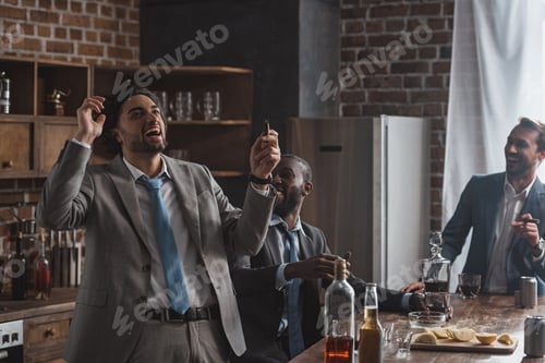 Preview: excited young businessmen smoking cigars and drinking alcoholic beverages together