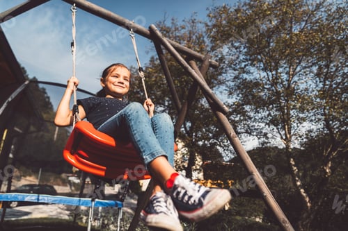 Preview: Low angle view of young caucasian girl playing on a swing outside on a sunny summer day