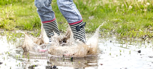 Preview: A child in rubber boots jumps in a puddle.