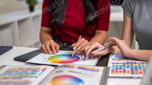 Preview: Close up of a woman and coworker holding pencil pointing on color chart sitting at table in office.