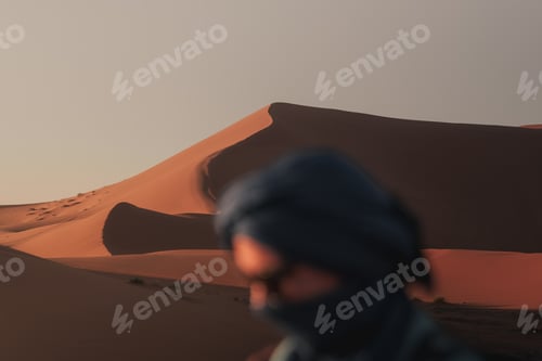 Preview: Blurred portrait of a berber man wearing a turban with the majestic dunes of erg chebbi at sunset
