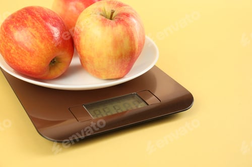 Preview: Electronic kitchen scale with apples on yellow background, closeup