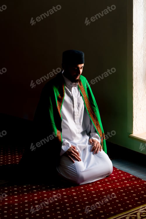 Preview: A Muslim believer prays in the twilight by a window in a mosque kneels down puts his forehead