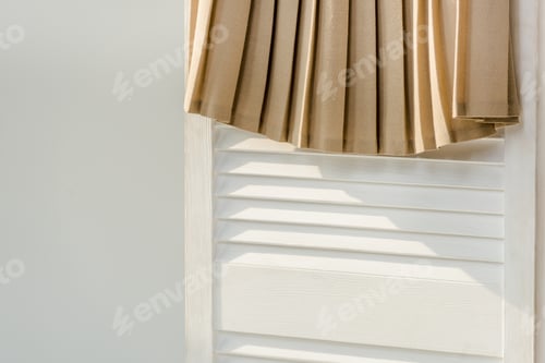 Preview: close up of beige pleated skirt hanging on white room divider isolated on grey
