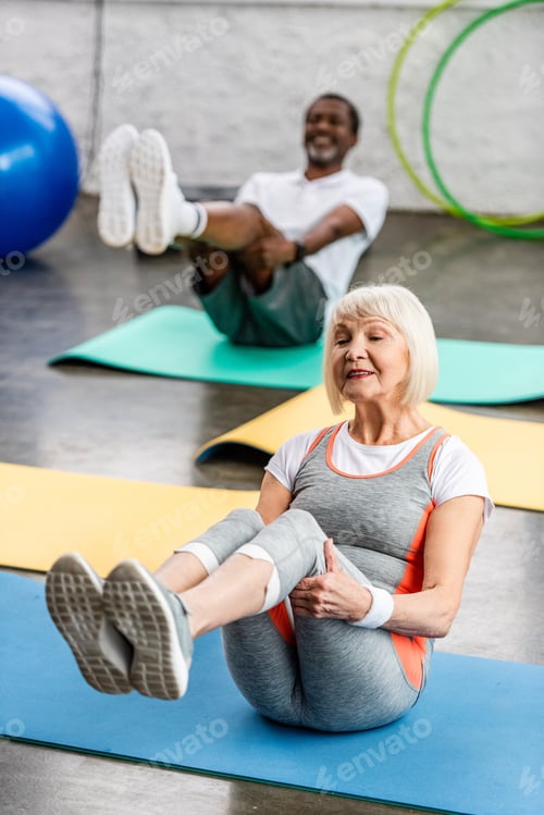 Preview: selective focus of senior woman and her husband exercising on fitness mats at gym
