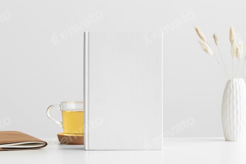 Preview: White book mockup with a lagurus and workspace accessories on a white table.