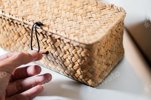Preview: Hand reaching for a woven basket with a black string latch